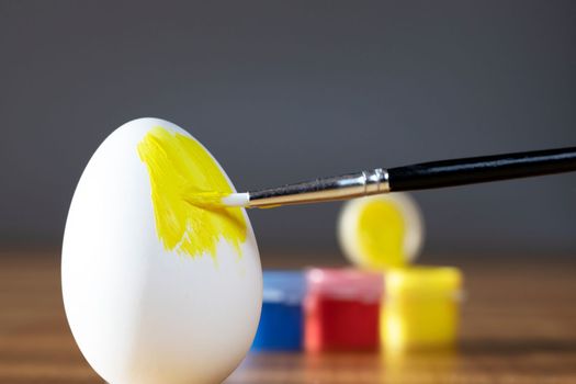 rough brush is painting a fragile easter egg with Yellow color, prepering for Holiday Happy Easter concept closeup colorful hobby