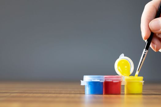 Artist paint brush with colorful paint on wooden table with gray background, copy space blue, red and yellow close up