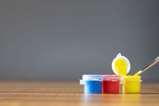 Artist paint brush with colorful paint on wooden table with gray background, copy space blue, red and yellow close up