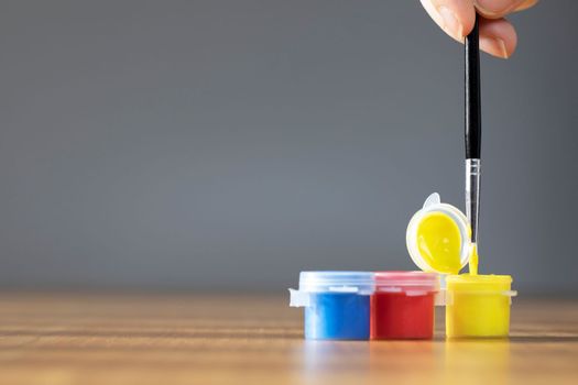 Artist paint brush with colorful paint on wooden table with gray background, copy space blue, red and yellow close up