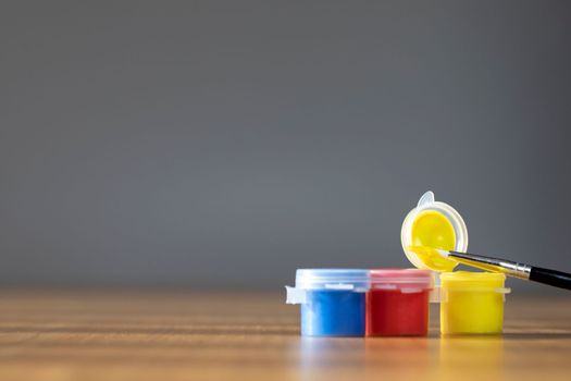 Artist paint brush with colorful paint on wooden table with gray background, copy space blue, red and yellow close up