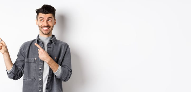 Happy handsome man smiling and pointing left at banner, showing cool product, standing on white background.