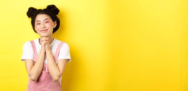 Stylish asian girl with bright makeup, say thank you, smiling grateful, standing happy on yellow background.