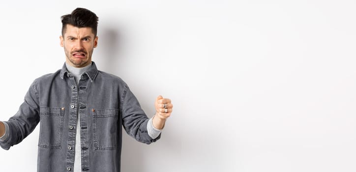 Disgusted guy showing big size object and grimacing from dislike and aversion, talking about disgusting large thing, standing on white background.