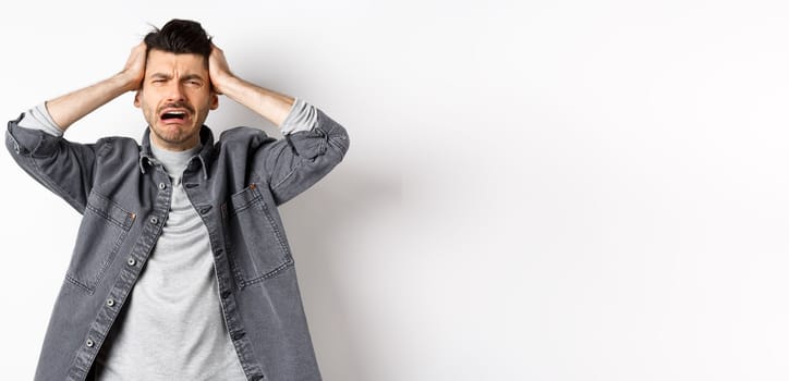 Frustrated guy crying and panicking, holding hands on head and screaming distressed, having trouble, standing upset on white background.