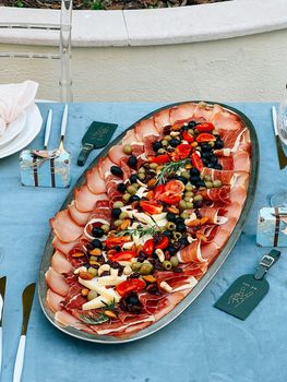 Oval dish with cheese and meat slices stands on a served table. High quality photo