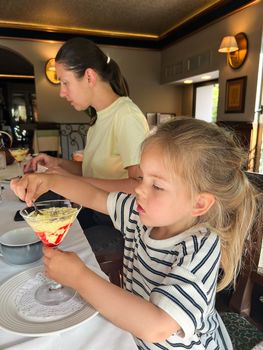 Little girl eating popsicles from a glass cup in a restaurant at the table. High quality photo