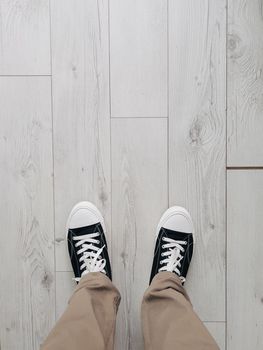 Male legs in black sneakers stand on a gray wooden floor. High quality photo
