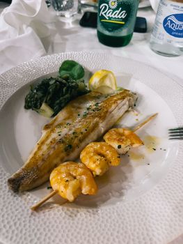Baked fish fillet and shrimp on a skewer lie on a plate. High quality photo