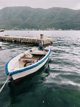 Fishing boat with a motor is moored at the pier in the rain against the backdrop of the mountains. High quality photo