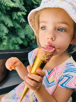 Little girl biting a popsicle waffle cone while sitting on a bench. High quality photo