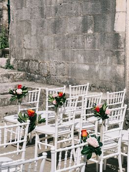 Rows of white flower-decorated chairs stand against an antique stone wall. High quality photo