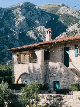 Pots of flowers hang on the terrace of an old stone house at the foot of the mountains. High quality photo