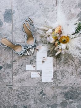 Wedding bouquet stands on a tile next to the bridal shoes, invitations and a ring. High quality photo