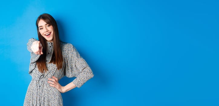 Motivated and excited young woman pointing finger at camera and smiling, congratulating you, praising or inviting, standing happy on blue background.