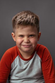 Preschool boy smiling with smirk at camera. Portrait of funny child on gray background. Emotions concept.