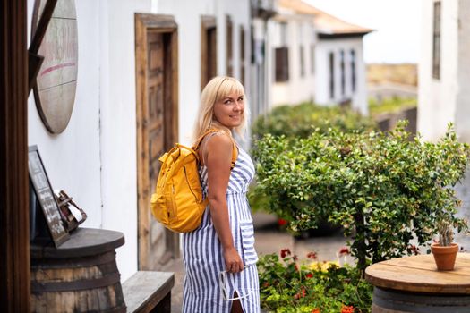 a blonde in a sundress with a backpack walks along the street of the Old town of Garachico on the island of Tenerife.Spain, Canary Islands