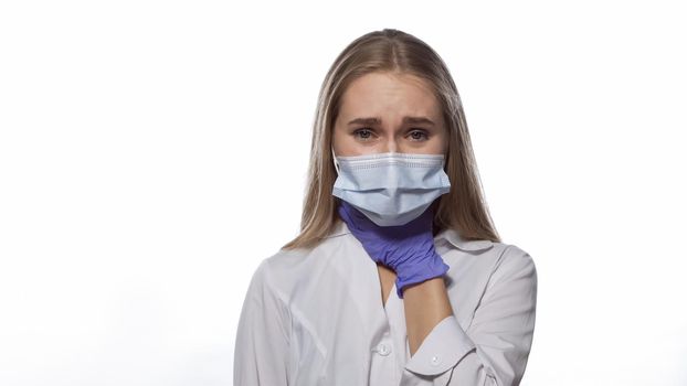 Sore throat nurse in a medical mask and disposable gloves touching her throat, looking at camera with pain in her eyes. Isolated on white background. Medicine concept.