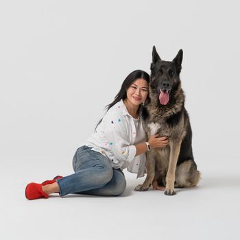 Beautiful woman hugs thoroughbred Shepherd dog. Happy brunette sitting with dog pet on floor. Cut out on white background.