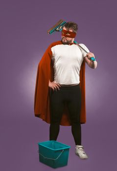 Super hero cleaner professional. Confidence man in red superhero costume with bucket and a mop stands on grape purple background. Super cleaning concept.