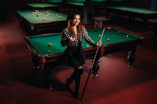 A girl in a hat in a billiard club with a cue in her hands.billiards Game.