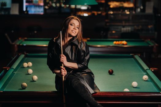 A girl with a cue in her hands sits on a table in a billiard club.Russian billiards.