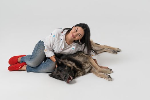 Smiling Asian woman lying in embrace with shepherd dog. Isolated on white background. Favorite pets concept.