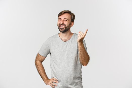 Image of handsome bearded man smiling and shaking finger to praise you, laughing over something funny, standing over white background.