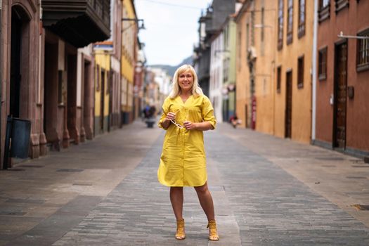 a blonde woman in a yellow summer dress stands on the street of the Old town of La Laguna on the island of Tenerife.Spain, Canary Islands.