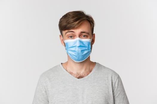 Concept of pandemic, covid-19 and social-distancing. Close-up of skeptical guy in medical mask, raising eyebrow and looking unamused, standing over white background.