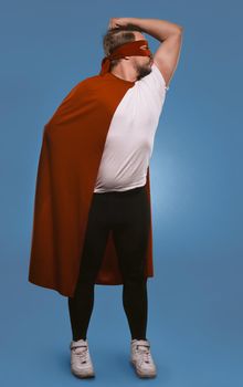 Super hero man ready to save world. Serious man shows and kisses his muscles standing in red super hero mask and coat. Cut out on faded denim blue background.