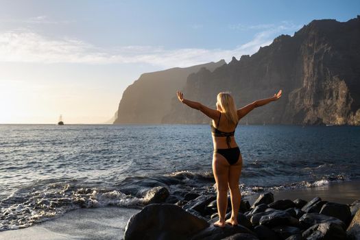 A girl at sunset on the beach near the cliffs of Acantilados de Los Gigantes at sunset, Tenerife, Spain