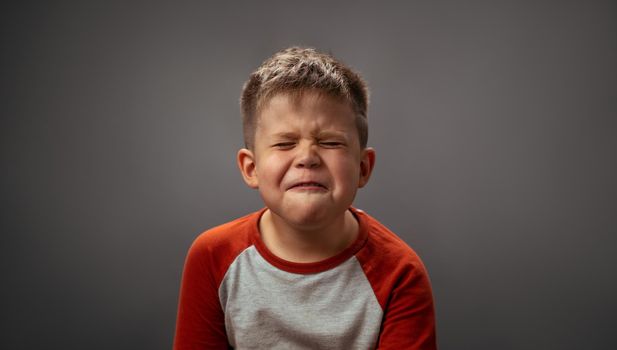 Little kid grimaces and closed his eyes. Preschool boy expresses unwillingness to brush his teeth. Emotions concept.