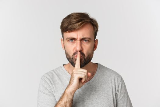 Close-up of angry caucasian man, shushing, telling to be quiet, frowning mad, standing over white background.