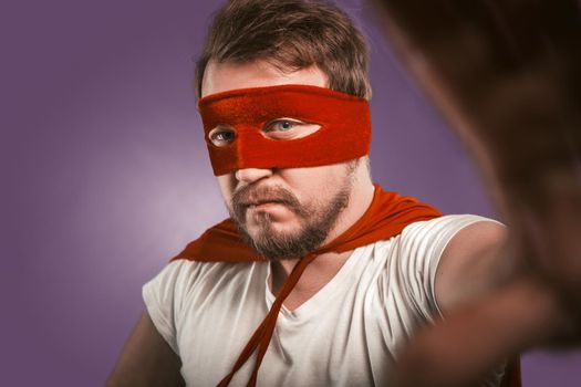 Superhero makes selfie photo by mobile phone for his blog, fans and followers. Close up portrait of serious man wearing red mask and cloak looking at camera.