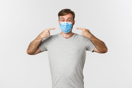 Concept of pandemic, coronavirus and social-distancing. Image of handsome man in gray t-shirt, recommending to wear medical masks during covid-19, white background.