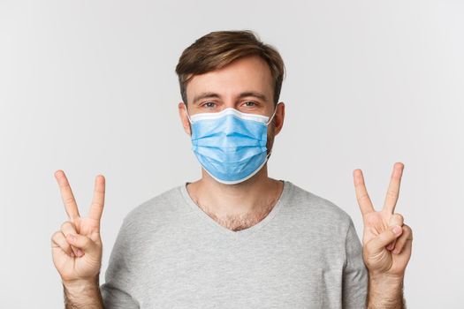 Concept of pandemic, coronavirus and social-distancing. Excited handsome man in gray t-shirt and medical mask, showing thumbs-up and smiling, liking something good.