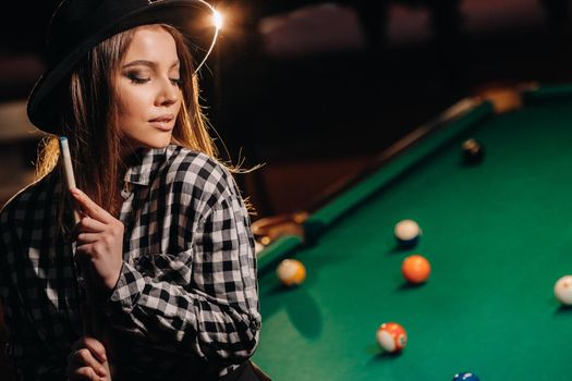 A girl in a hat in a billiard club with a cue in her hands.billiards Game.