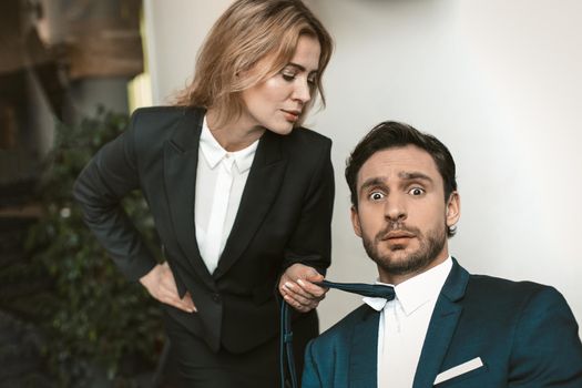 Pretty businesswoman seduces her male boss or collegue. Caucasian female holding tie of businessman. Sexual harassment concept.