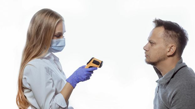 A young nurse looks at the display of a thermometer monitor and checks the body temperature of visitors or office workers. Isolated on white background.