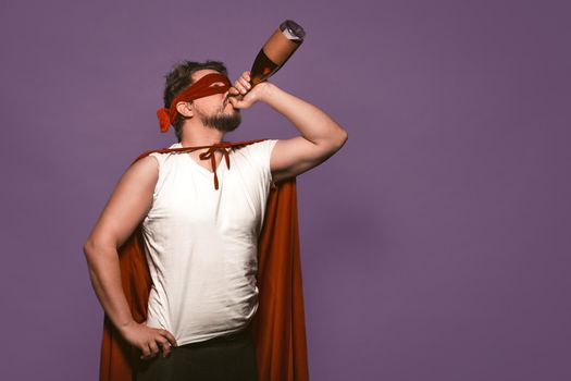 Super antihero man drinks alcohol from the throat of a bottle. Isolated on grape purple background with copy space or textspace at right side.