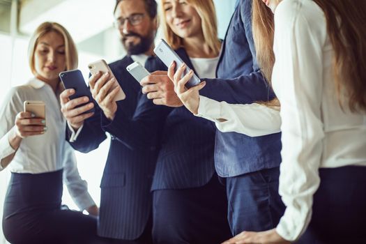 Group of smiling business people holding mobile phones and looking on its. Toned image.