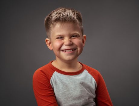 Happy preschool boy expresses joy. Smiling broadly child cut out on gray. Studio portrait. Emotions concept.