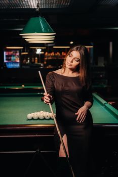 A girl in a hat in a billiard club with a cue in her hands.Pool Game.