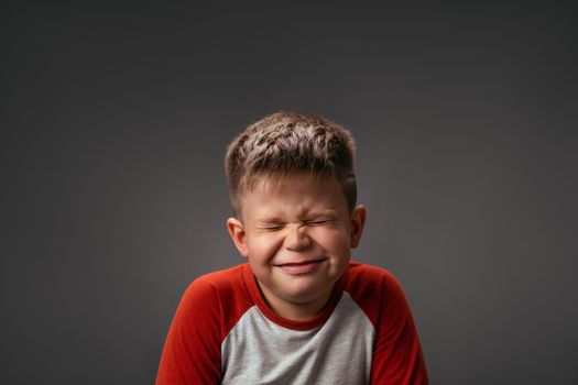 Funny boy smiles closed eyes. Isolated on gray background. Birthday surprise concept. Emotions concept. Copy spaces at both sides.