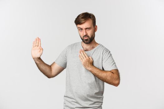 Funny bearded man in gray t-shirt, showing martial arts skills and pouting, standing over white background.