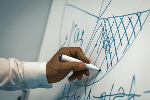 Businessman draws diagram with marker on white board. Close up shot of male hand. Toned image.