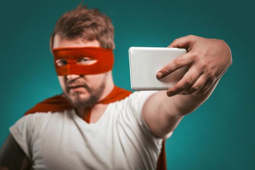 Super hero blogger man makes selfie photo or video on mobile phone for his blog or story on social networks. Isolated on biscay green background. Focus on hand with phone.
