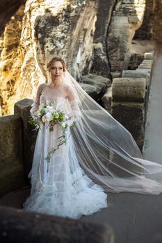 A bride in a white dress with a bouquet of flowers on the background of mountains and gorges in the Swiss Saxony, Germany, Bastei.