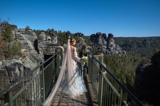 A bride in a white dress with a bouquet of flowers on the background of mountains and gorges in the Swiss Saxony, Germany, Bastei.